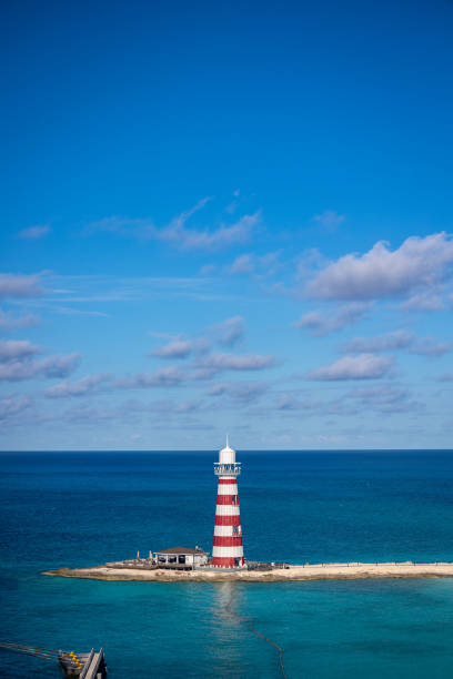 Stereotypical light house building with red and white stripes on a background of puffy clouds