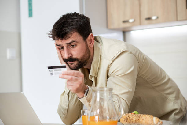 istock Confused young man in PJs looking at his credit card 1395206258