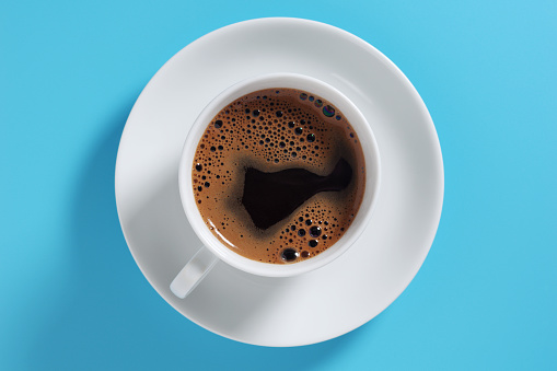 Cup of coffee on blue background, top view