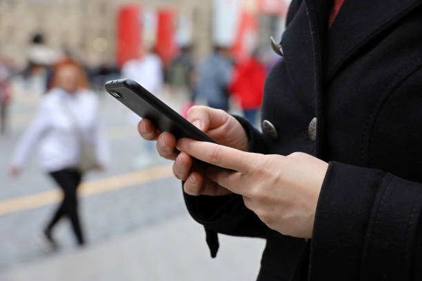 istock Female hands with smartphone close up on blurred people background 1395207051