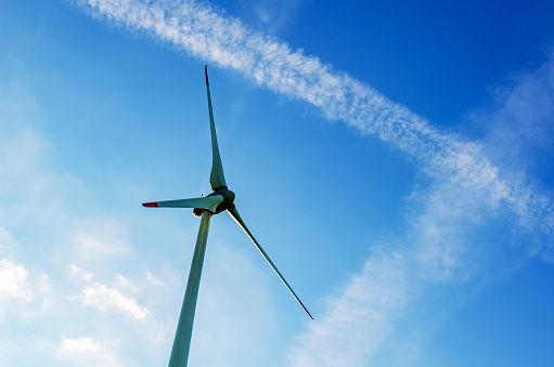 Rotor of a wind turbine against blue sky with contrails