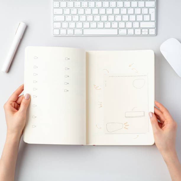 Top view of workspace with keyboard, mouse, marker and female hands holding notebook stock photo