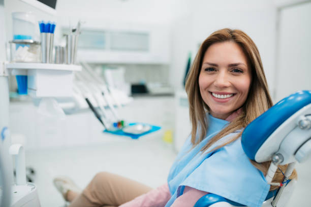 Happy woman visiting a dentist office Portrait of a young happy woman with a long hair and a wide toothy smile, comfortably sitting on a dentist chair and having a blue cloth cover on her, looking at camera dentists office stock pictures, royalty-free photos & images