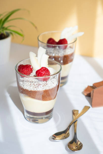 istock Delicious three-layer mousse, vanilla, chocolate, creme brulee dessert in a glass in the bright rays of the sun. Nearby are pieces of milk chocolate. 1395214009