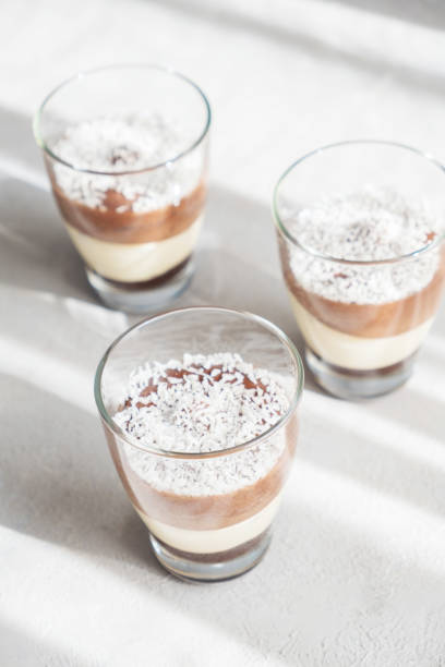 istock Three-layer chocolate and vanilla mousse dessert in glass cups, sprinkled with coconut flakes, on a children's serving board. brunch. 1395214093