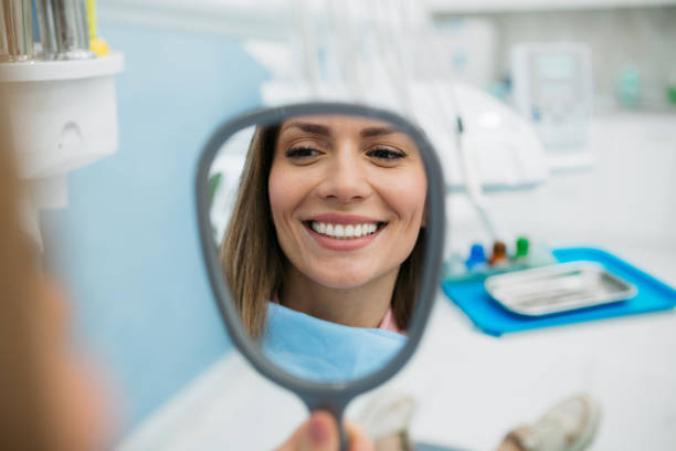 a happy woman looking herself in the hand held mirror - dentist imagens e fotografias de stock