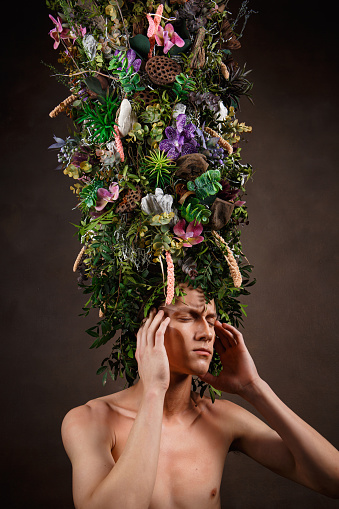 A man with a huge elongated headdress made of living diverse vegetation and flowers. A child of nature, a fabulous creature.