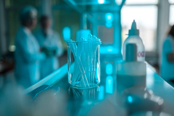 Plastic pipettes in a glass jar on a lab shelf. Blue light passing through the transparent materials. Blurred background.