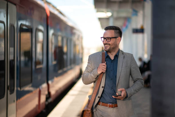 młody biznesmen korzystający z telefonu komórkowego na dworcu kolejowym zdjęcie stockowe... - business travel zdjęcia i obrazy z banku zdjęć