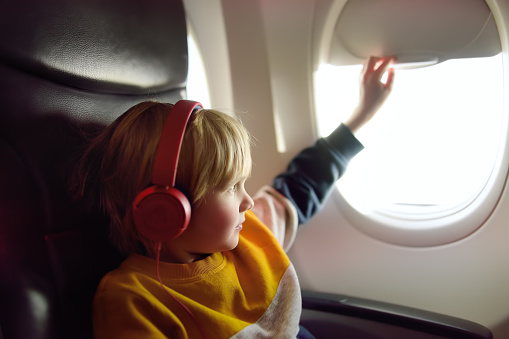 Cute little boy traveling by an airplane. Child using player to listen a music or audiobook during the flight. Entertainment for family with kids on a board of plane