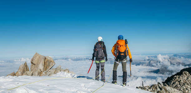 istock Couple connected team rope  with climbing harness dressed mountaineering clothes with backpacks and ice axes enjoying views ascending Mont Blanc (Monte Bianco) summit near Aiguille du Midi, France. 1395228341