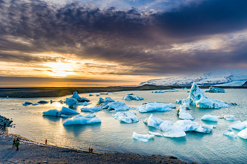 People watching icebergs in a beautiful glacial lagoon at sunset (Jokusarlon, Iceland)
