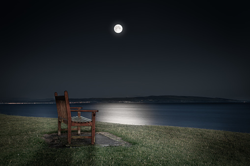 Public bench with distant view over the sea in the moonlight near Troon Pier, East Ayrshire, Scotland, UK