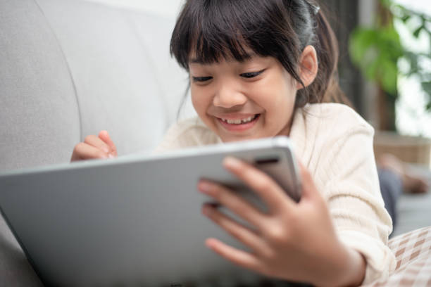 istock Little girl using tablet playing game on the internet, Kid sitting on sofa watching or talking with a friend online, Child relaxing in living room in the morning, Children with New Technology concept 1395239712