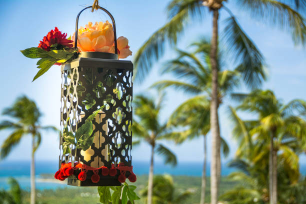 Candle holder hanging with flowers a background of palm trees.