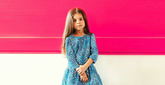 Portrait of beautiful little girl child wearing blue dress on pink background