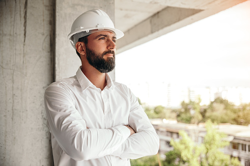 Serious male entrepreneur in hardhat crossing arms and looking away while visiting construction site