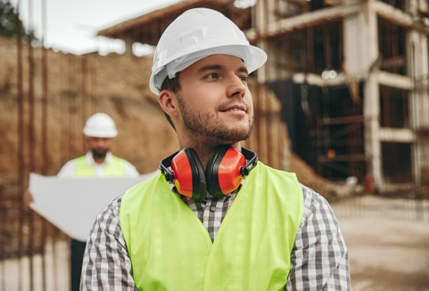 istock Smiling young male contractor standing at construction site and looking away 1395253590