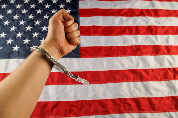 istock caucasian hand cuffed with silver metal handcuffs over US flag background 1395254152