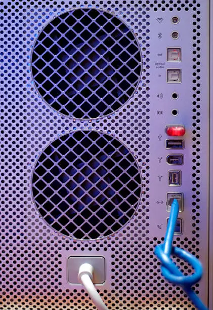 Back of last generation computer with all conectors, fans, network cable with knot plugged in.  Blue light reflection gives lab / scientific environment.