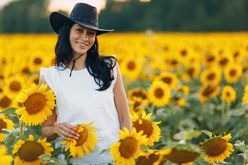 Beautiful young woman in hat on sunflower field.