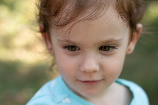 Portrait of a beautiful young girl in a blue t-shirt on a blurred green natural background. Outdoor photo