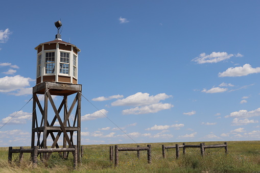 The guard tower at Amache National Historic Site, a Japanese Internment Camp, rises high above the green grass around it on a bright, sunny day.