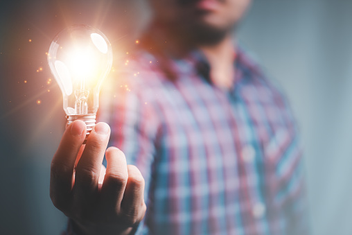 Idea innovation and inspiration concept. Hand of man holding illuminated light bulb, concept creativity with bulbs that shine glitter. Inspiration of ideas for sustainable business development.