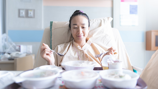 Asian woman lying on the hospital bed for admitting and she is eating breakfast. Hospitalization concept.