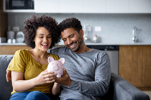 Happy couple at home holding a piggy bank with their savings and smiling - home finances concepts