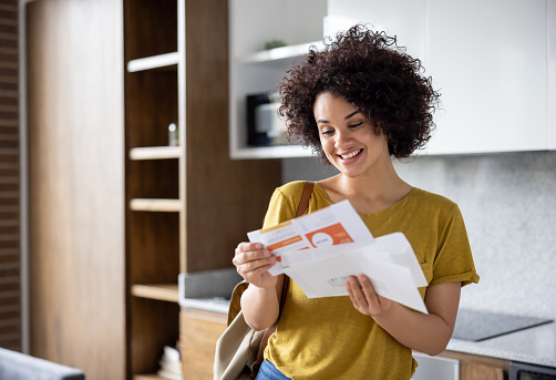 Happy Latin American woman checking the mail while arriving home and smiling - domestic life concepts