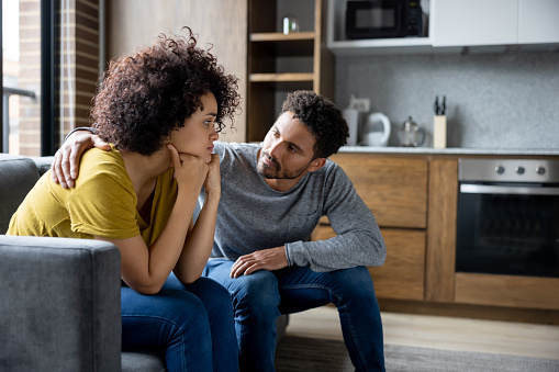 African American man comforting his girlfriend at home while she is looking upset - lifestyle concepts