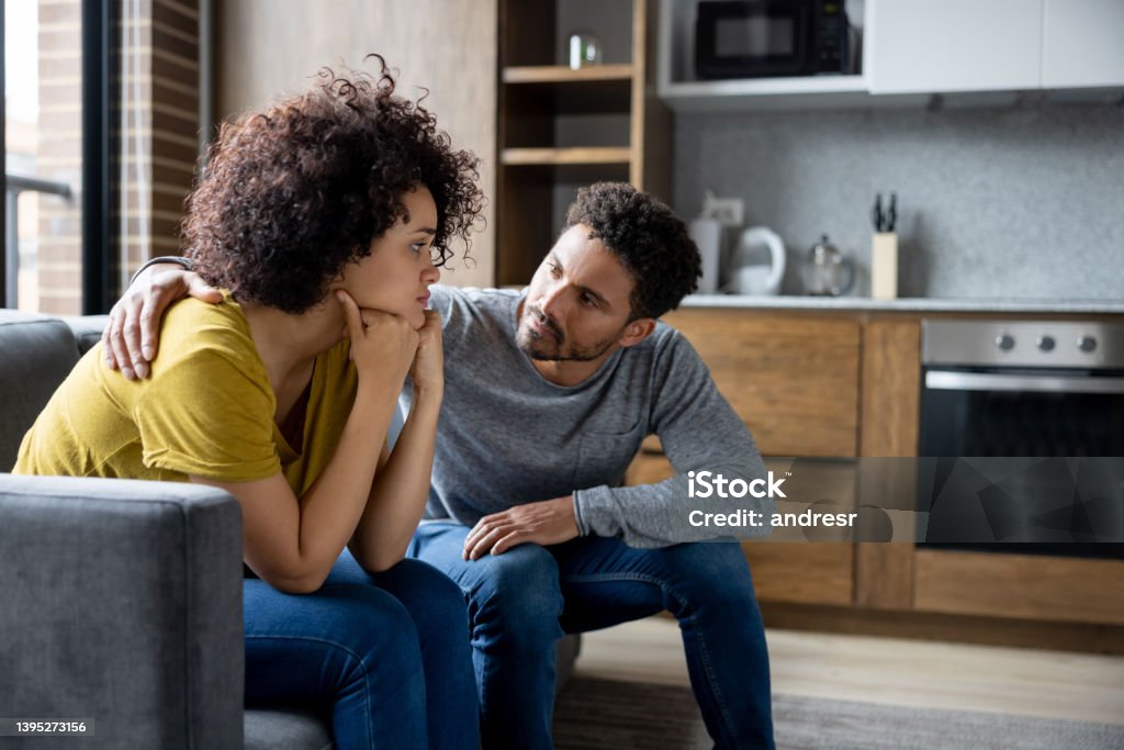 Man comforting his girlfriend at home African American man comforting his girlfriend at home while she is looking upset - lifestyle concepts Couple - Relationship Stock Photo