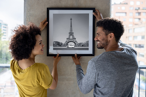 Couple hanging a framed picture on the wall at home - interior design concepts