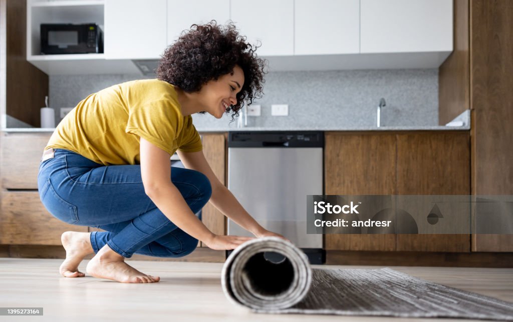 Happy woman decorating her house and unrolling a carpet Happy Latin American woman decorating her house and unrolling a carpet in the living room - domestic life concepts Rug Stock Photo