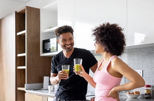 Fit Latin American couple drinking a green detox juice at home - Healthy eating concepts
