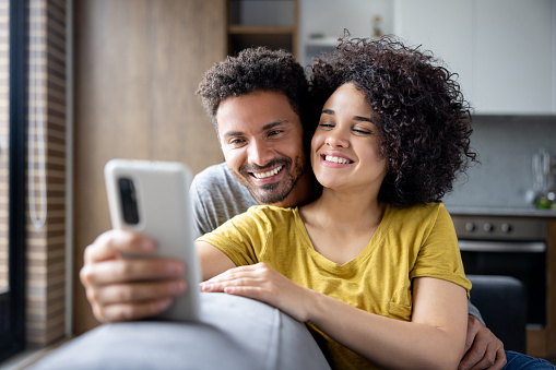 Happy Latin American couple watching funny videos at home on a cell phone and smiling