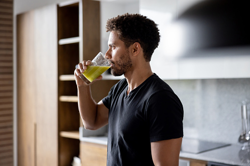 Fit African American man drinking a green juice for breakfast at home - healthy lifestyle concepts