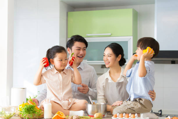 Family kitchen parentage. Young parents are teaching two preschoolers how to cook, children pick up sweet peppers as headphones. - stock photo stock photo