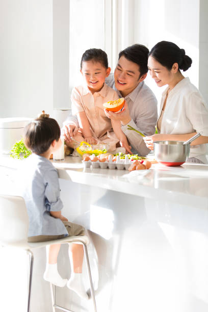 istock Young parents are playing with their kids while cooking, and their mischievous son is using the mushrooms on his head as a hat. - stock photo 1395275282