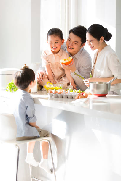 Young parents are playing with their kids while cooking, and their mischievous son is using the mushrooms on his head as a hat. - stock photo stock photo