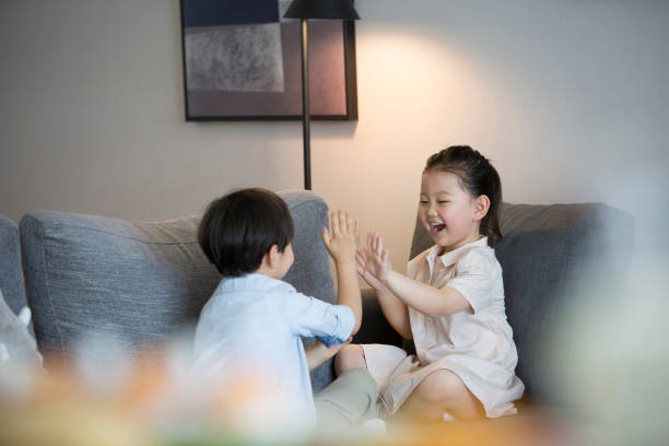 A little girl and a little boy are playing hand clapping on the living room sofa - stock photo stock photo