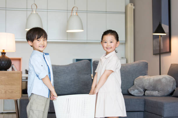 By the living room sofa, the siblings carry a white basket together - stock photo stock photo
