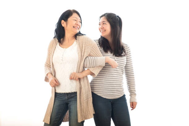 Mature Asian Mother Linking Arms with Eurasian Daughter, White Background Chinese mother and multiracial daughter portrait on white background. arm in arm stock pictures, royalty-free photos & images