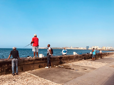 Havana, Cuba - June 20, 2019: Local cuban men fishing on a breakwater of Havana city.