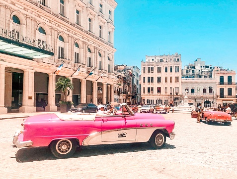 Man driving classic pink car next to Manzana hotel, Havana, Cuba. Editorial