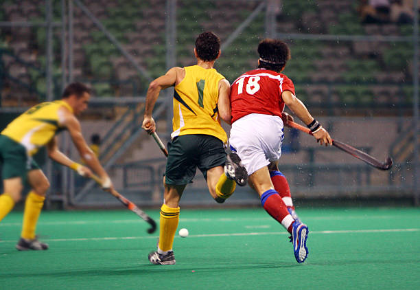 Three players playing hockey on a pitch Hockey in action. field hockey stock pictures, royalty-free photos & images