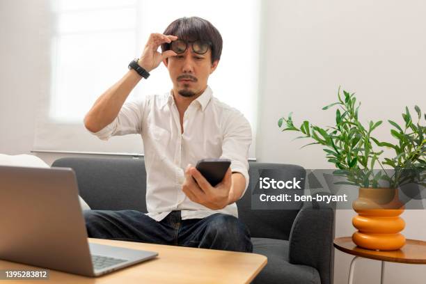 Asian Man Squint Eye To Look At The Phone Due To Long Eye Sighted Problems Stock Photo - Download Image Now