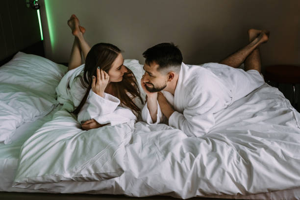 Happy couple having fun and joking looking each other on the bed of hotel stock photo