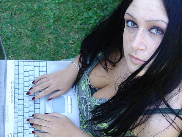 Girl sitting on the grass and working on her laptop stock photo